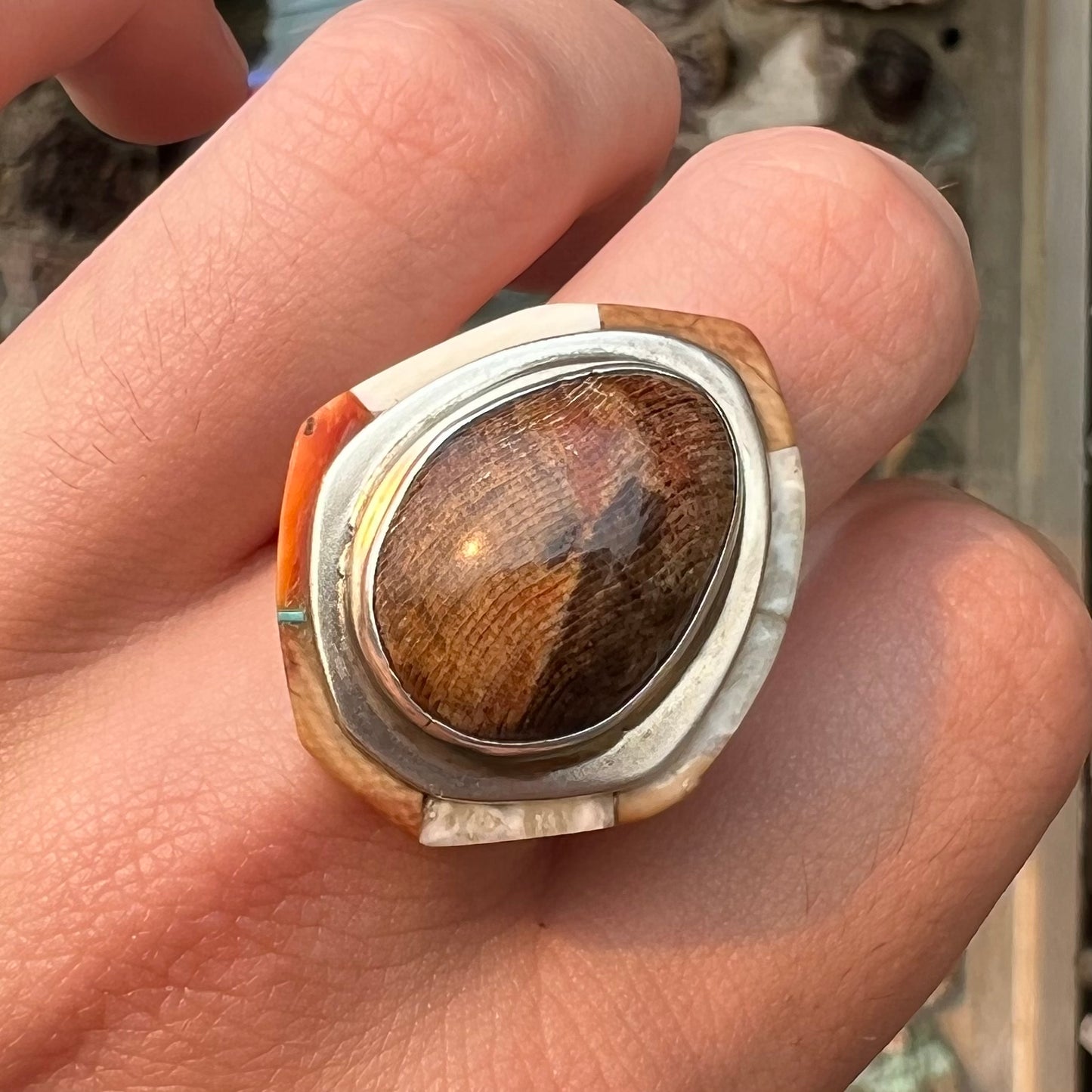 A silver ring handmade from a bezel set petrified wood stone, surrounded by quartz, carnelian, and bone inlay.