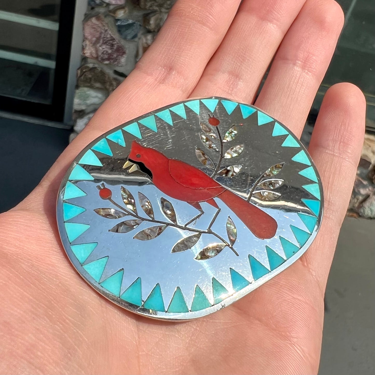 A Zuni belt buckle featuring a red cardinal inlaid with coral, handmade by artists Dennis and Nancy Edaakie.