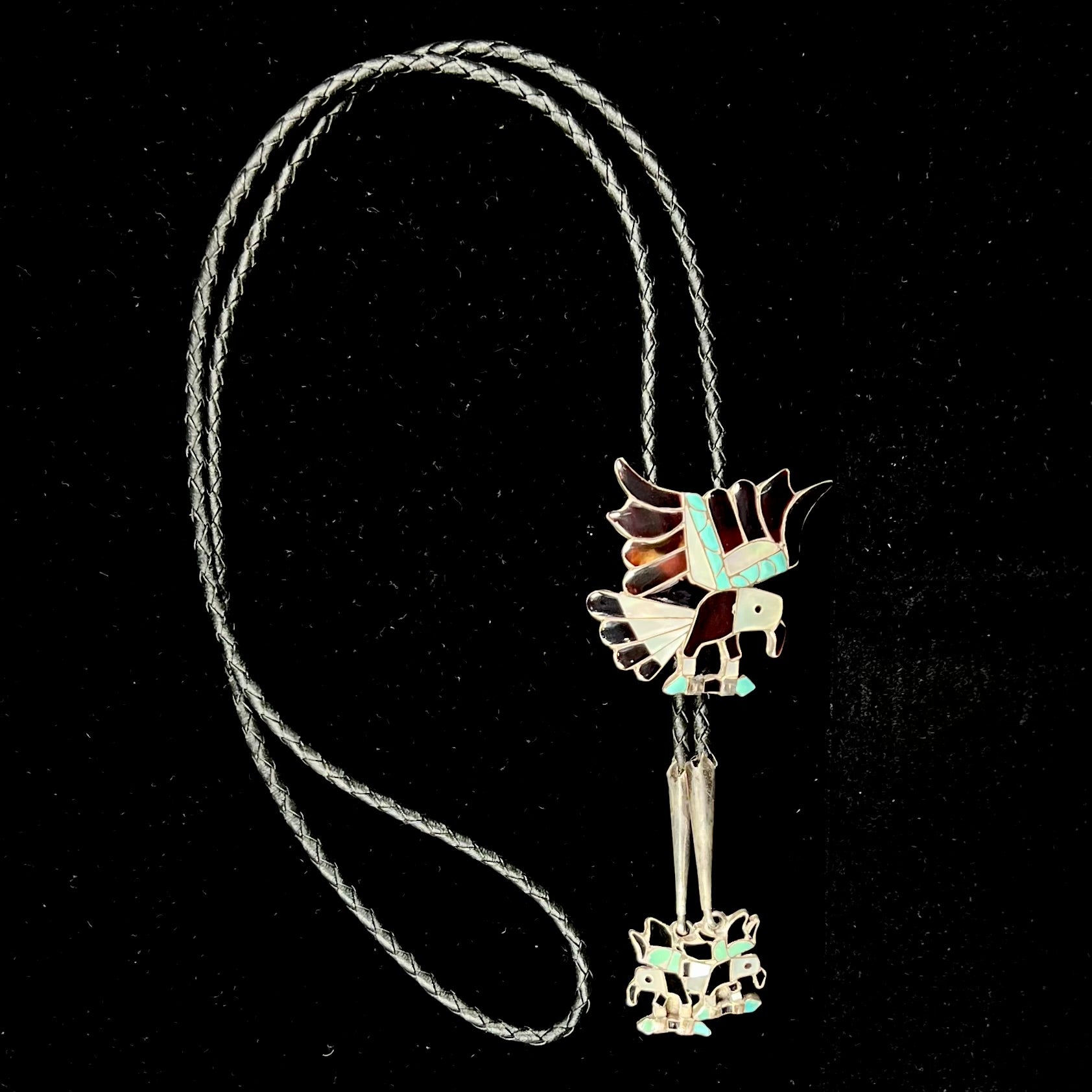A sterling silver Zuni Indian-made bolo tie featuring the motif of three flying eagles inlaid with natural stones.