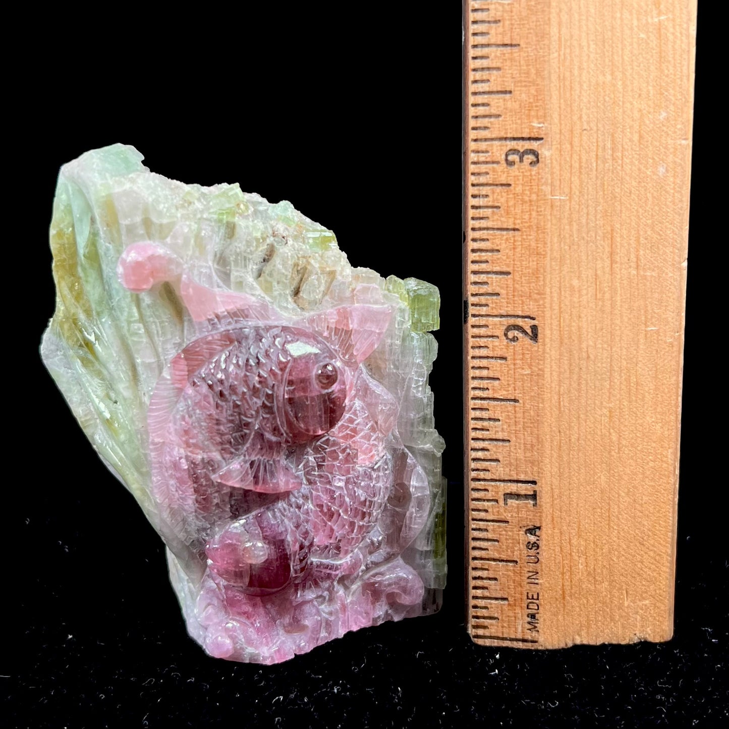 A stone carving of two fish swimming together carved from a watermelon tourmaline crystal conglomerate by artist, Ronald Stevens.