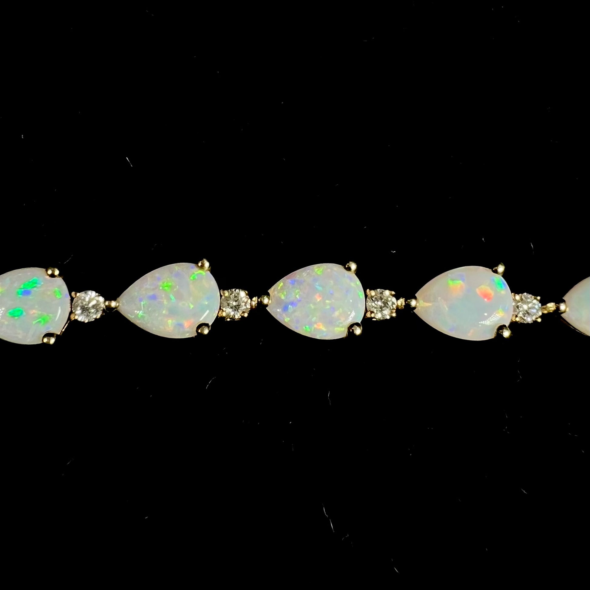 A ladies' gold tennis style bracelet set with pear shaped white crystal opals and diamonds.