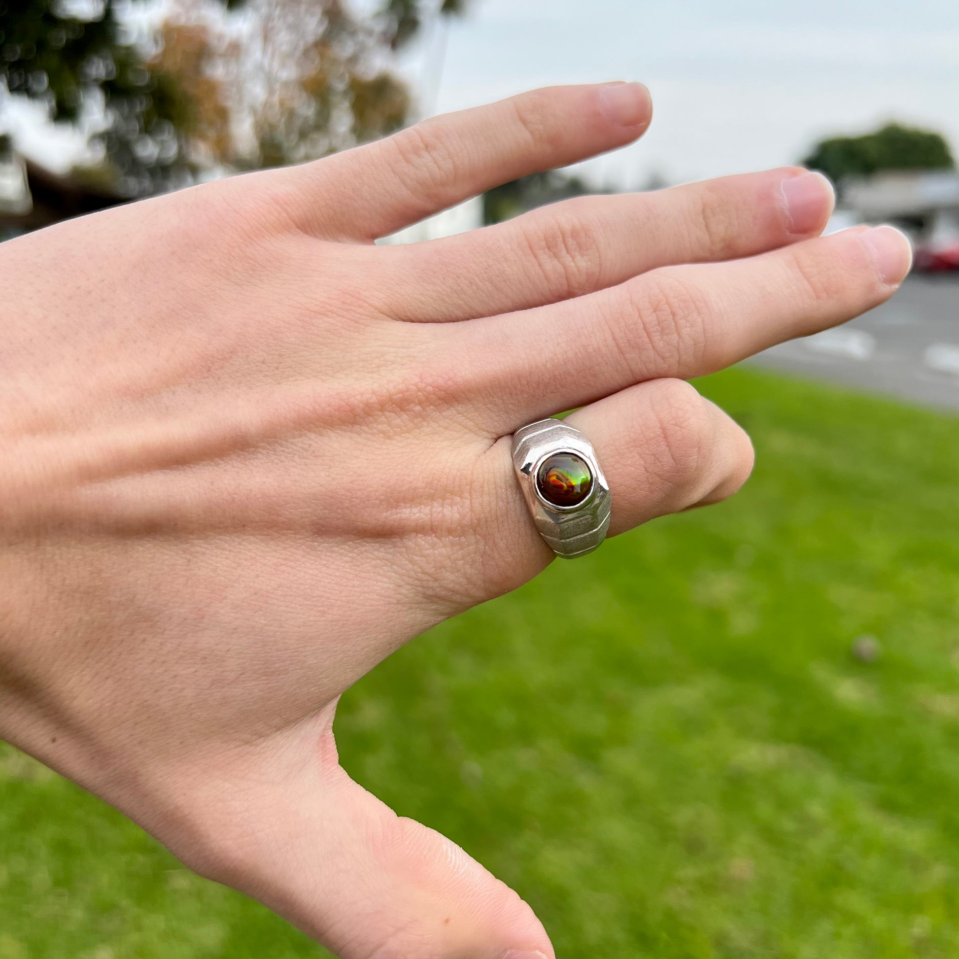 A round cabochon cut red and green fire agate set in a brushed metal white gold men's ring.