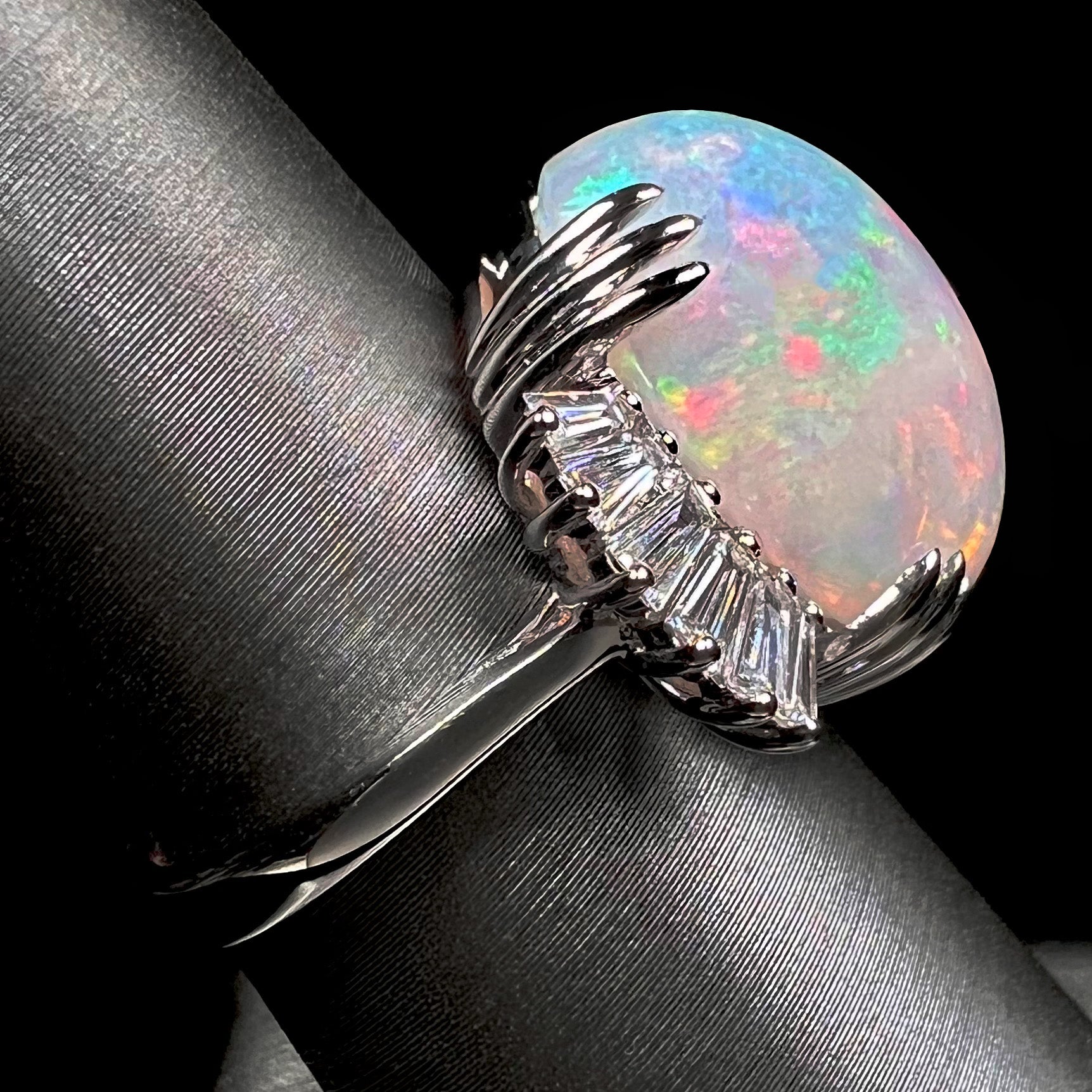 An oval cabochon cut opal mounted in a ladies' white gold ring between tapered baguette cut diamonds.