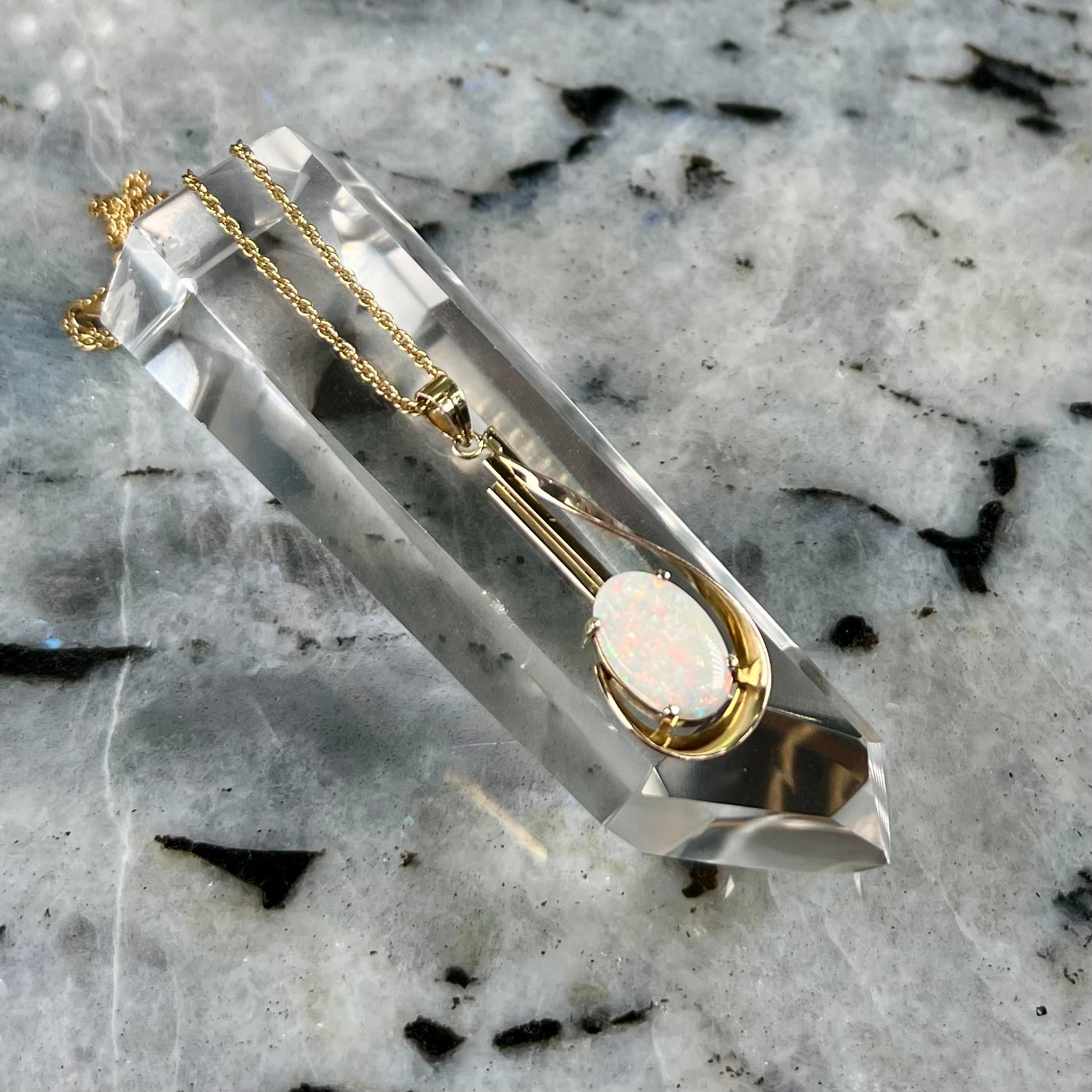 A handmade gold drop pendant set with an oval cabochon cut white crystal opal.