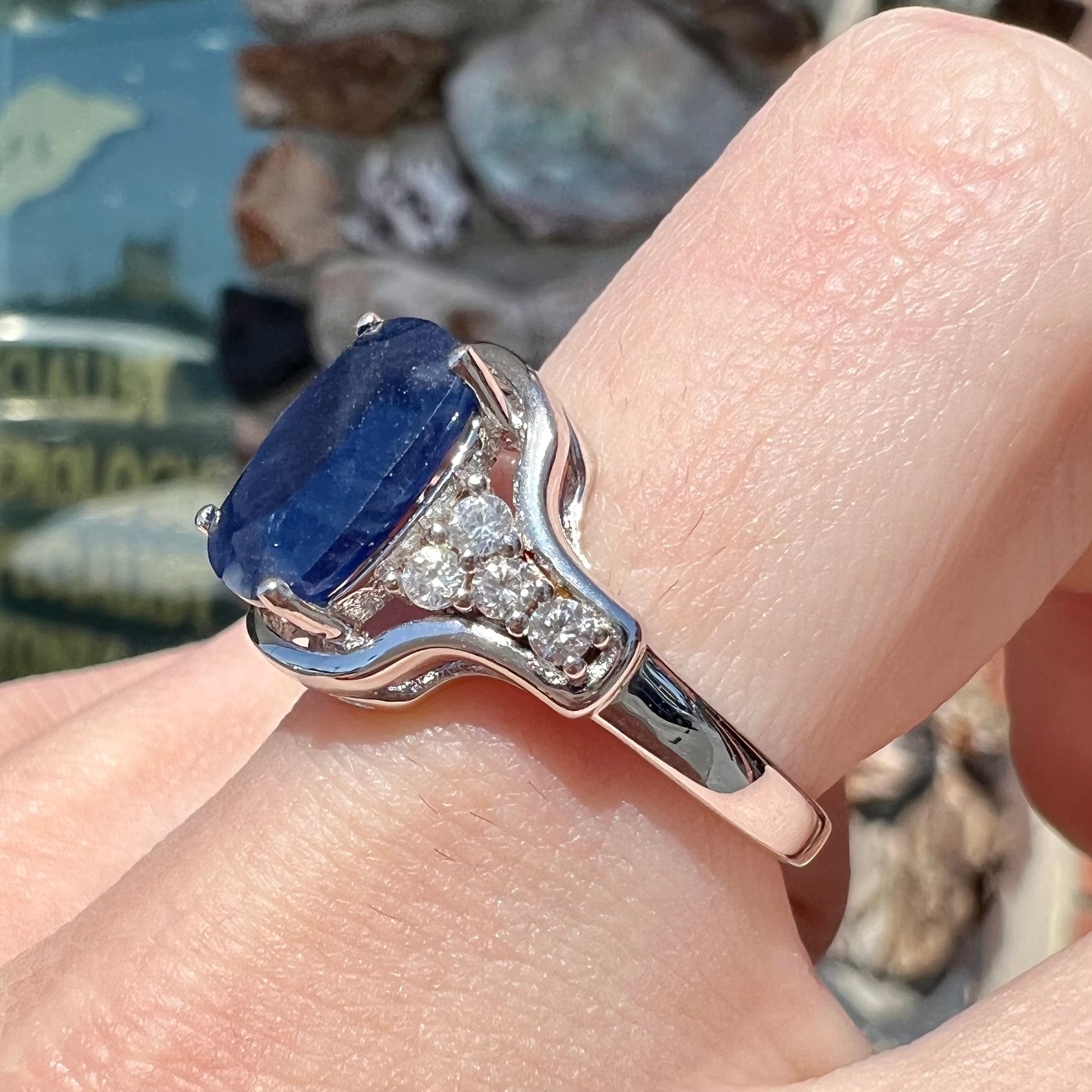 A sterling silver ring set with a cushion cut blue sapphire center stone and round cut white sapphire accents.