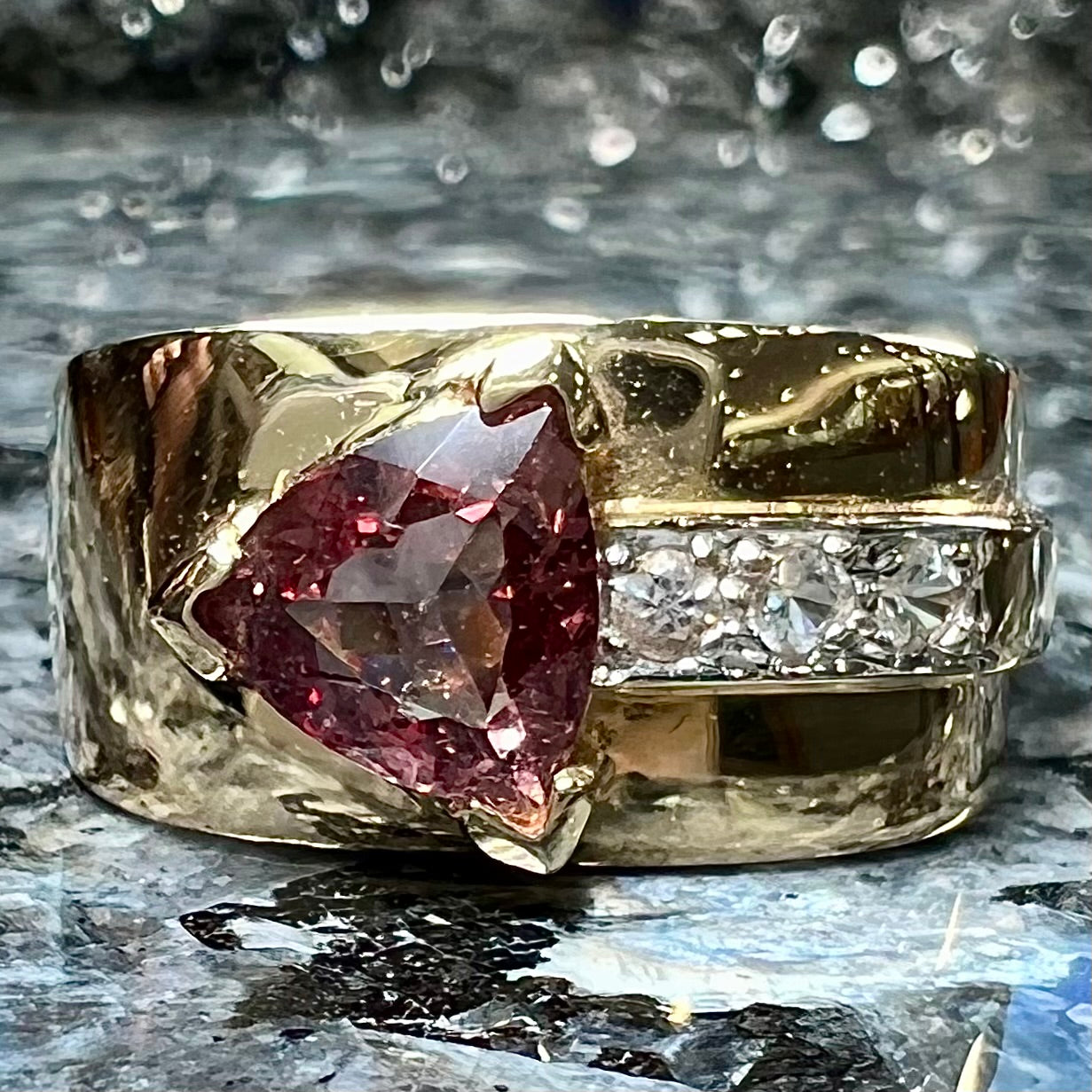 A men's gold pink tourmaline ring.  Set next to the trillion cut tourmaline is a row of three round white sapphires.