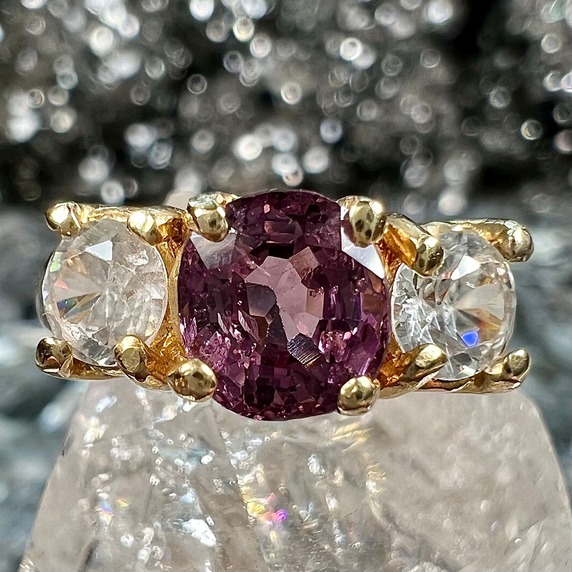 A yellow gold three stone ring set with two round cut white zircons and one cushion cut purple spinel.