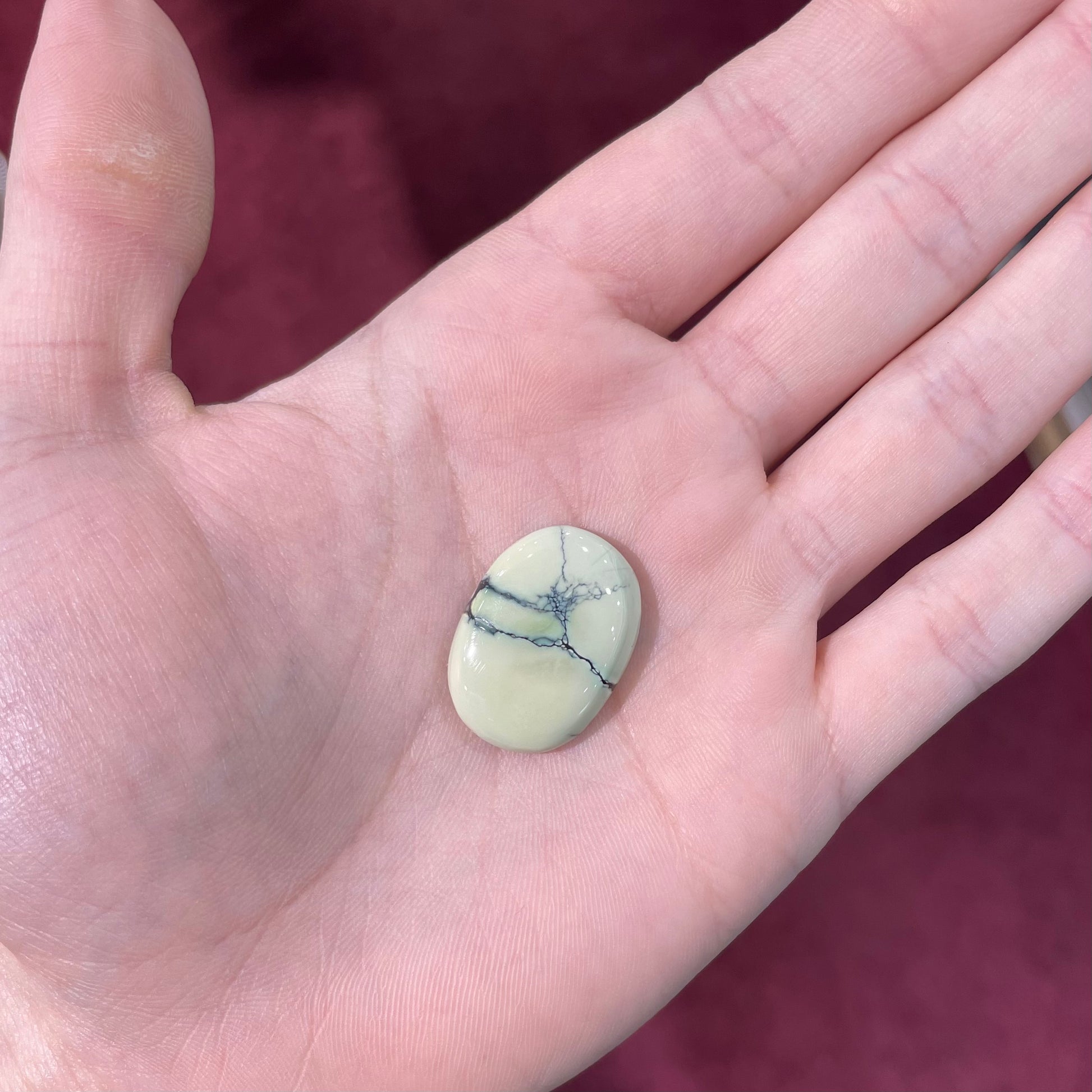 A loose, oval cabochon cut variscite stone from Utah, USA.  The stone is yellow-green with a black matrix.