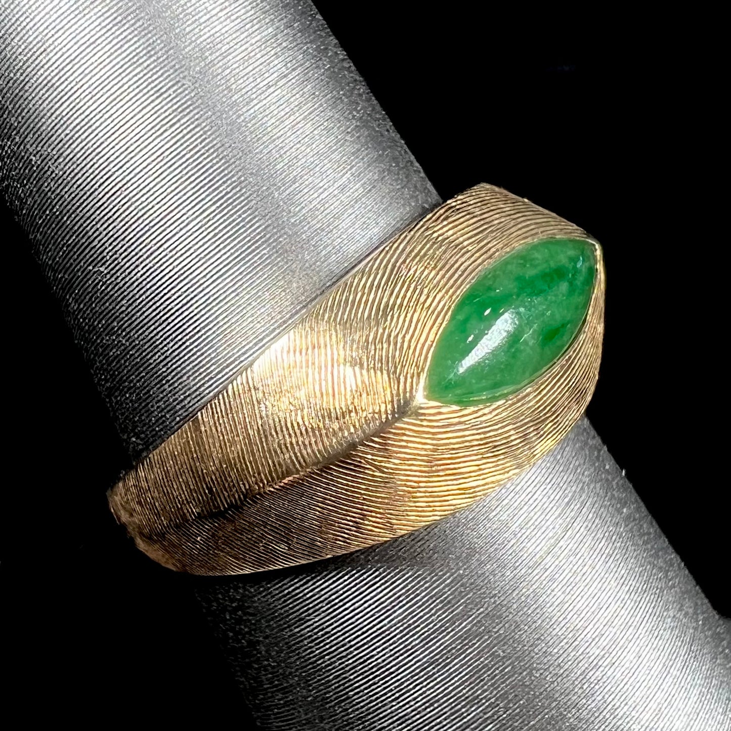 A textured yellow gold ring set with a marquise cabochon cut green jadeite stone.