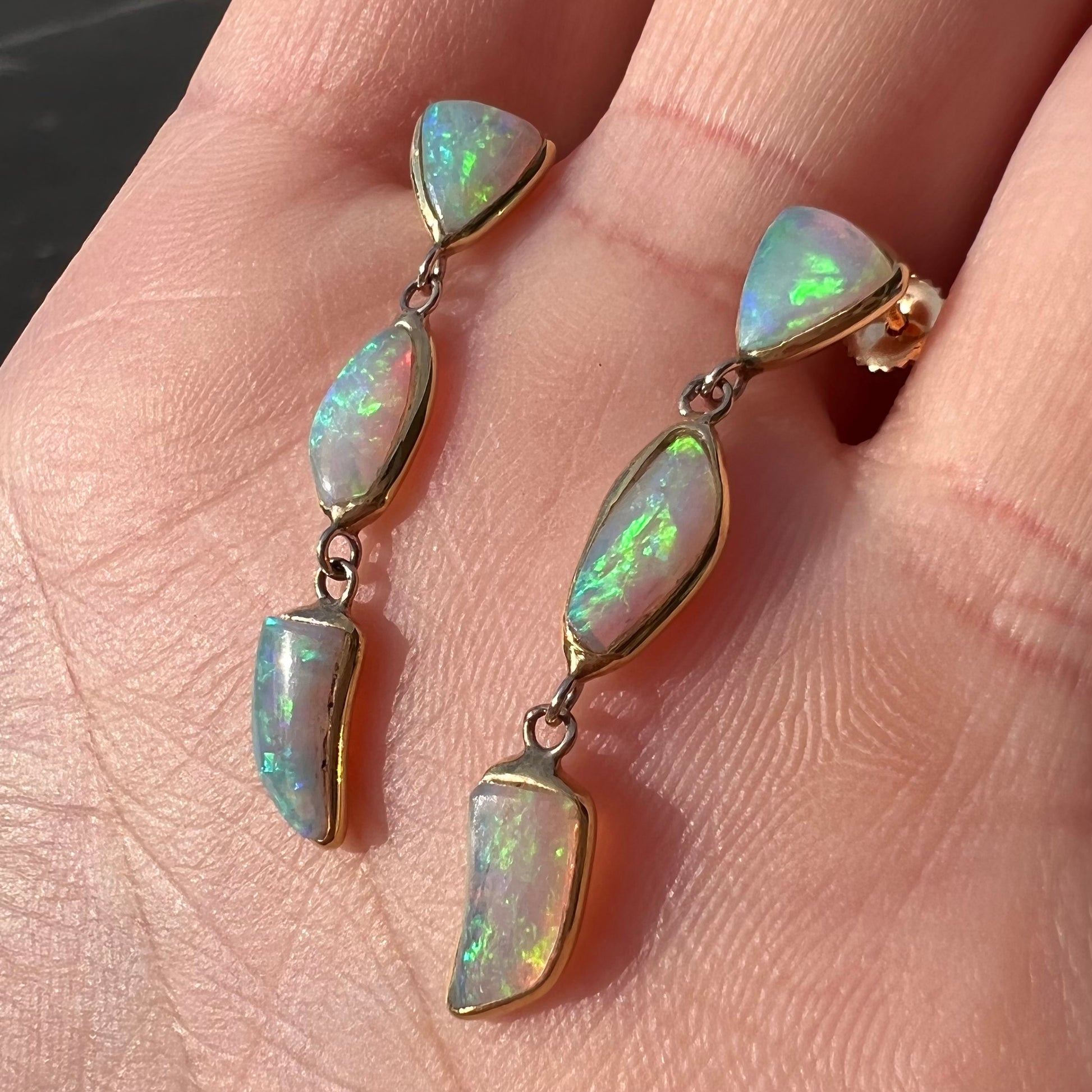 A pair of yellow gold push-back dangle earrings set with three white crystal opals in each.
