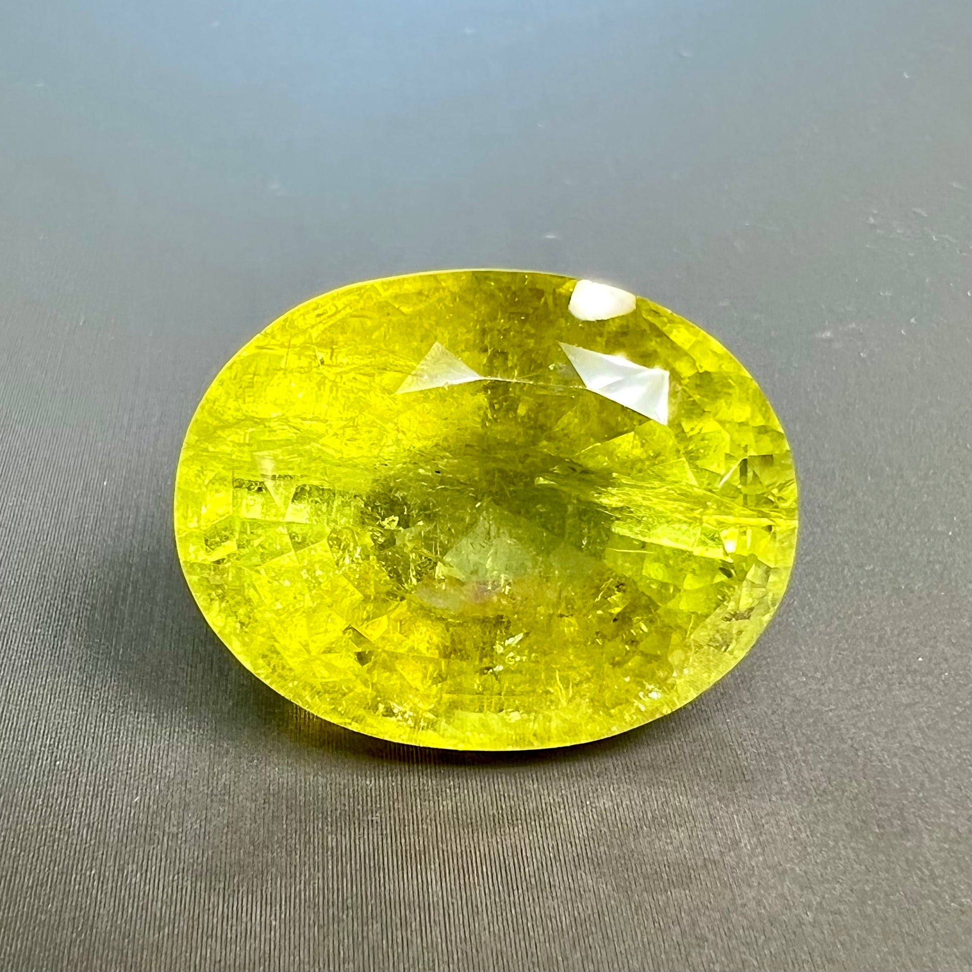 A loose, faceted oval cut green tourmaline stone.  The color is an almost neon yellow-green.