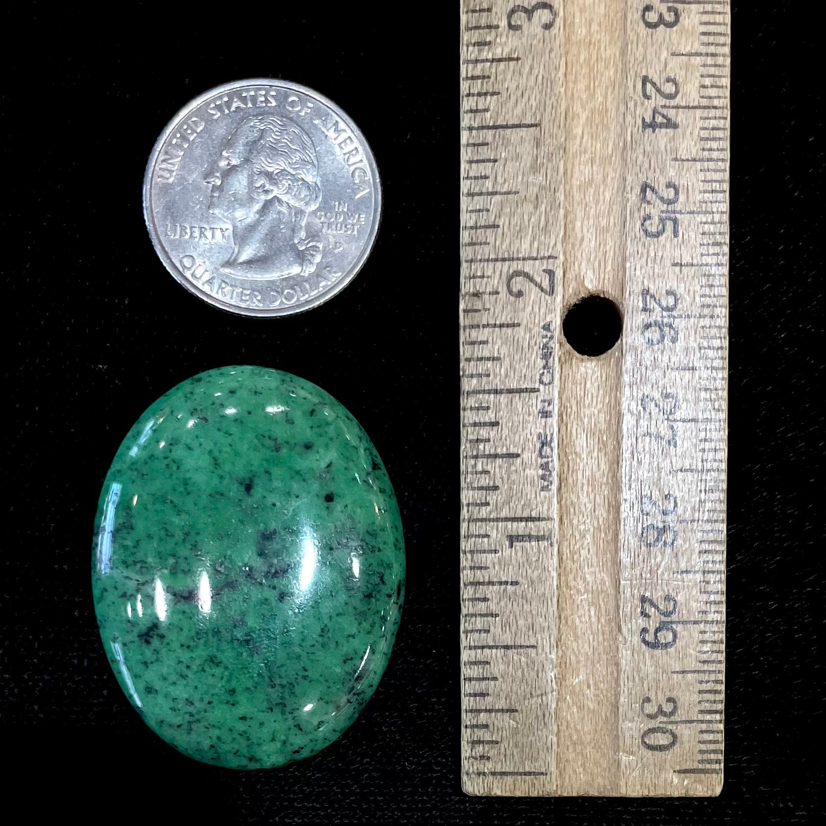A loose, oval cabochon cut green zoisite stone with black spots.