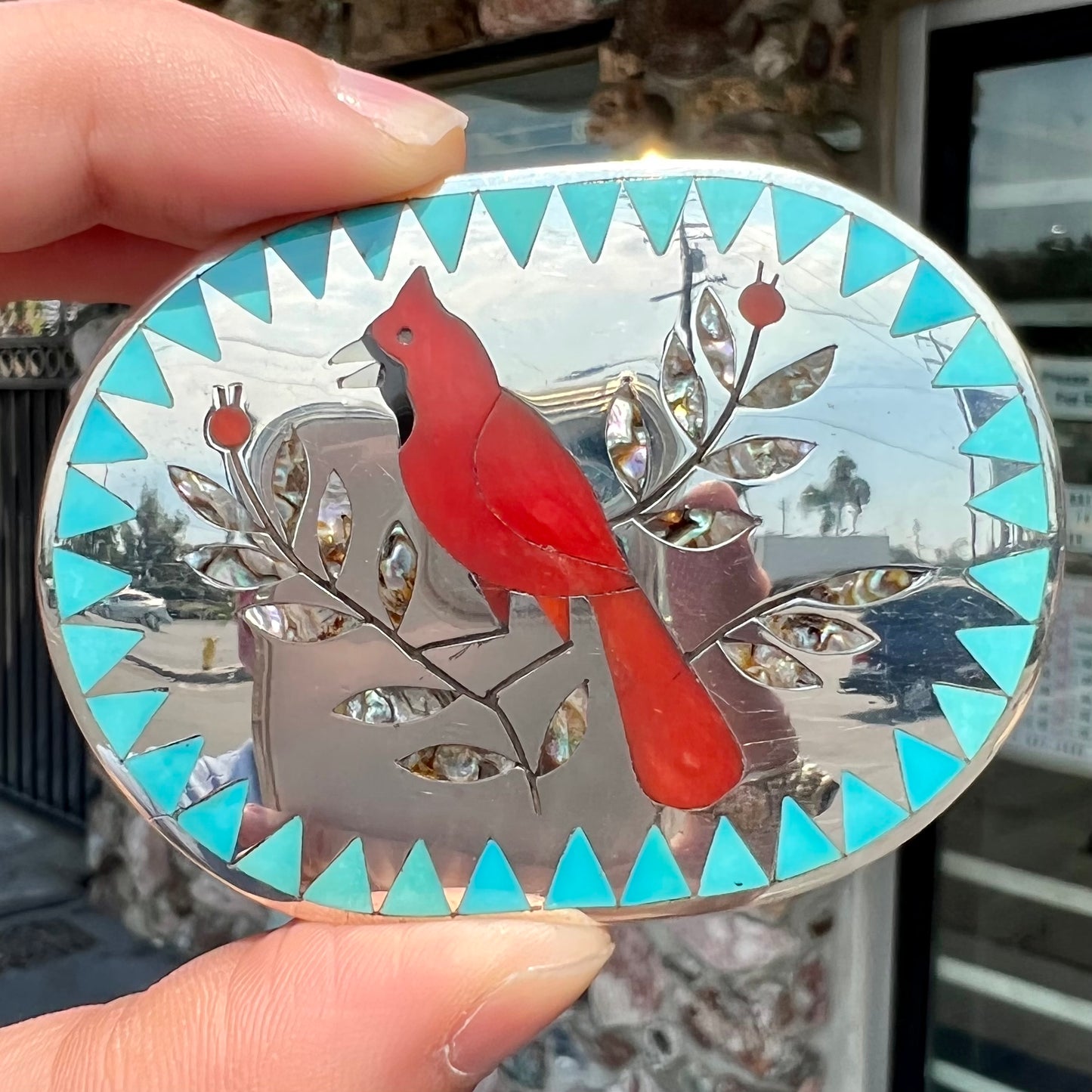 A Zuni belt buckle featuring a red cardinal inlaid with coral, handmade by artists Dennis and Nancy Edaakie.