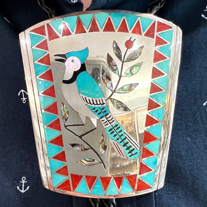 A turquoise and coral inlay bolo tie featuring the motif of a blue jay bird, handmade by Zuni artists Dennis and Nancy Edaakie.