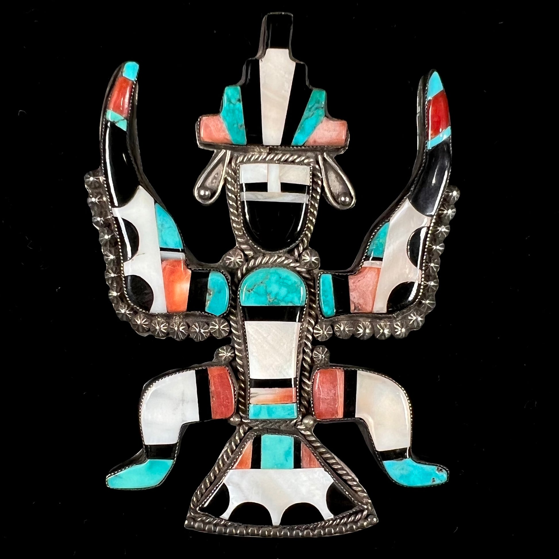 A silver, Zuni Indian dancing eagle necklace/pin.  The piece is inlaid with pieces of onyx, turquoise, coral, and mother of pearl.