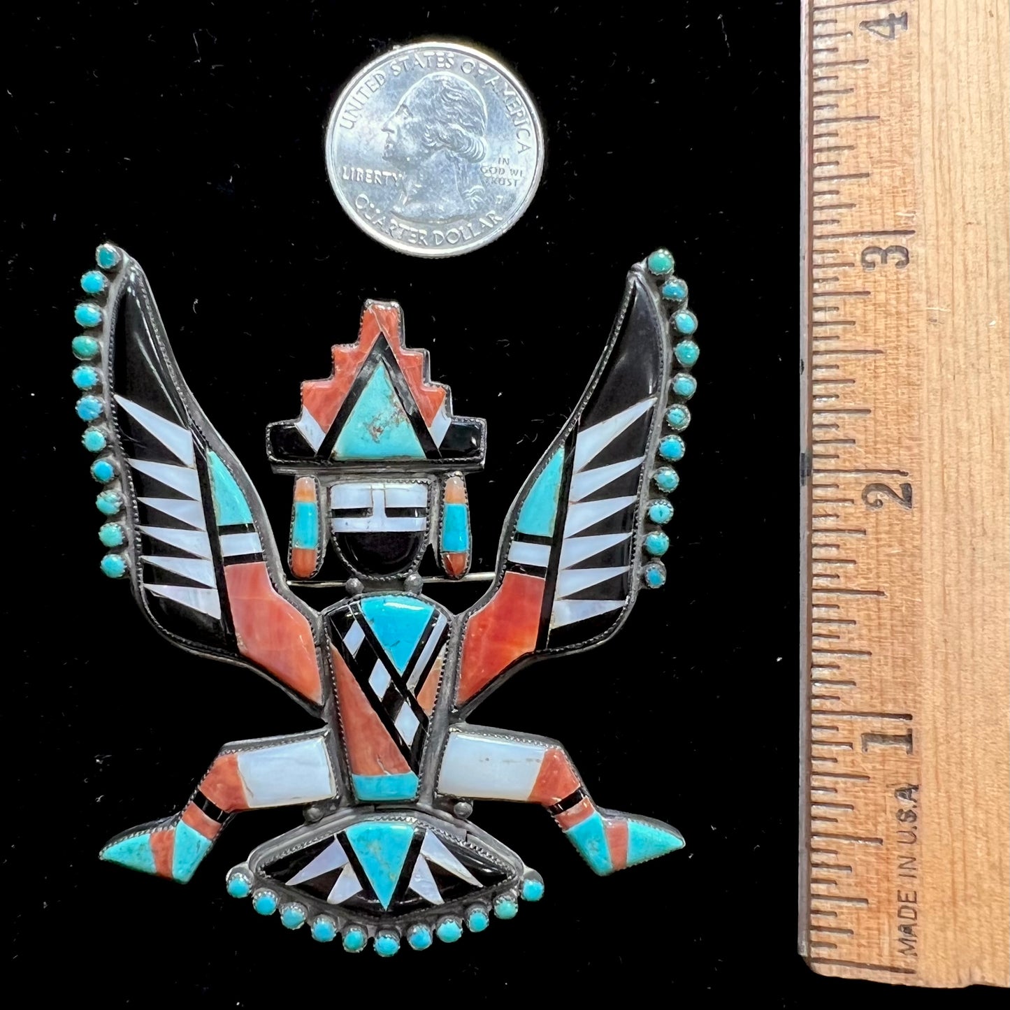 A handmade, silver Zuni dancing eagle pin.  The piece is inlaid with turquoise, coral, mother of pearl, and onyx stones.