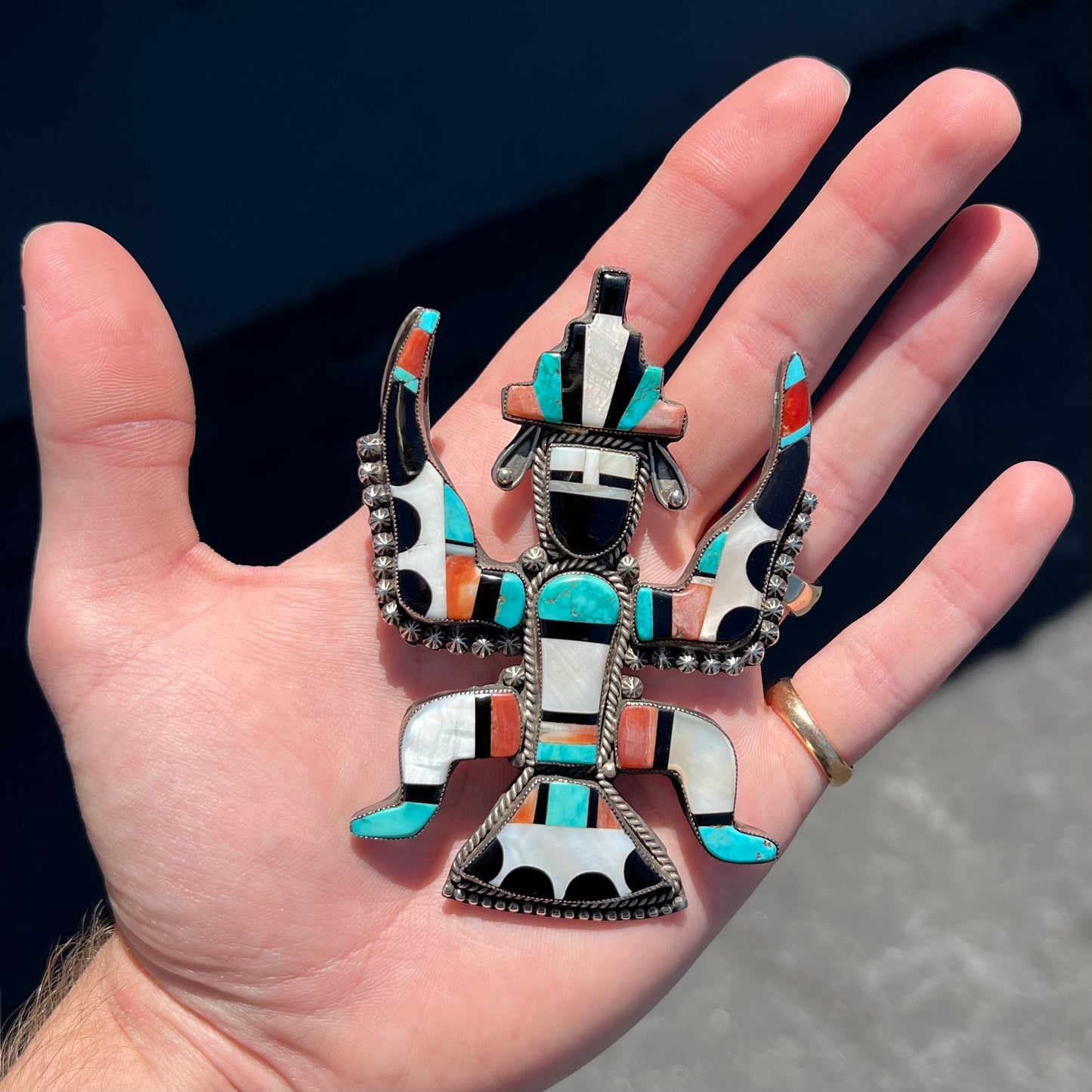 A silver, Zuni Indian dancing eagle necklace/pin.  The piece is inlaid with pieces of onyx, turquoise, coral, and mother of pearl.
