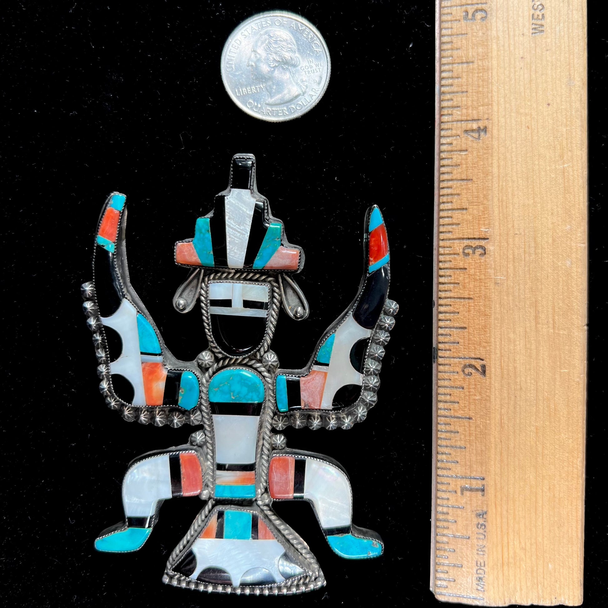 A silver, Zuni Indian dancing eagle necklace/pin.  The piece is inlaid with pieces of onyx, turquoise, coral, and mother of pearl.