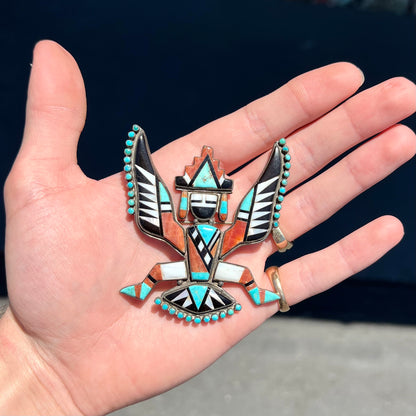 A handmade, silver Zuni dancing eagle pin.  The piece is inlaid with turquoise, coral, mother of pearl, and onyx stones.