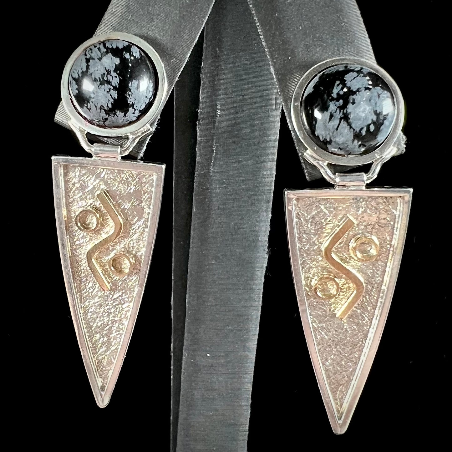 A pair of two-tone silver and gold snowflake obsidian earrings handmade by Zuni artist, Myron Panteah.