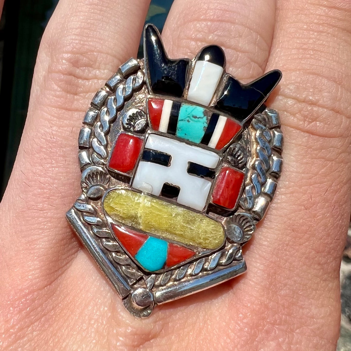 A sterling silver ring handmade in the motif of a Zuni Indian horned kachina set with onyx, turquoise, coral, mother of pearl, and sulfur quartz stones.