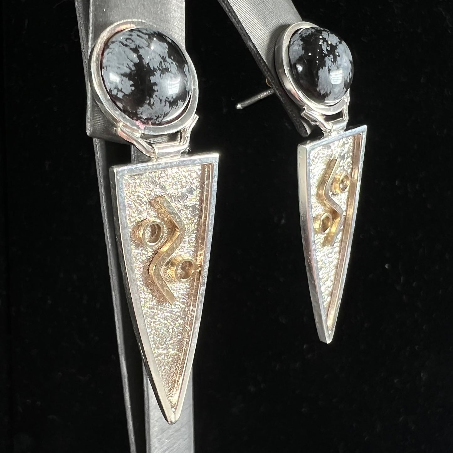 A pair of two-tone silver and gold snowflake obsidian earrings handmade by Zuni artist, Myron Panteah.