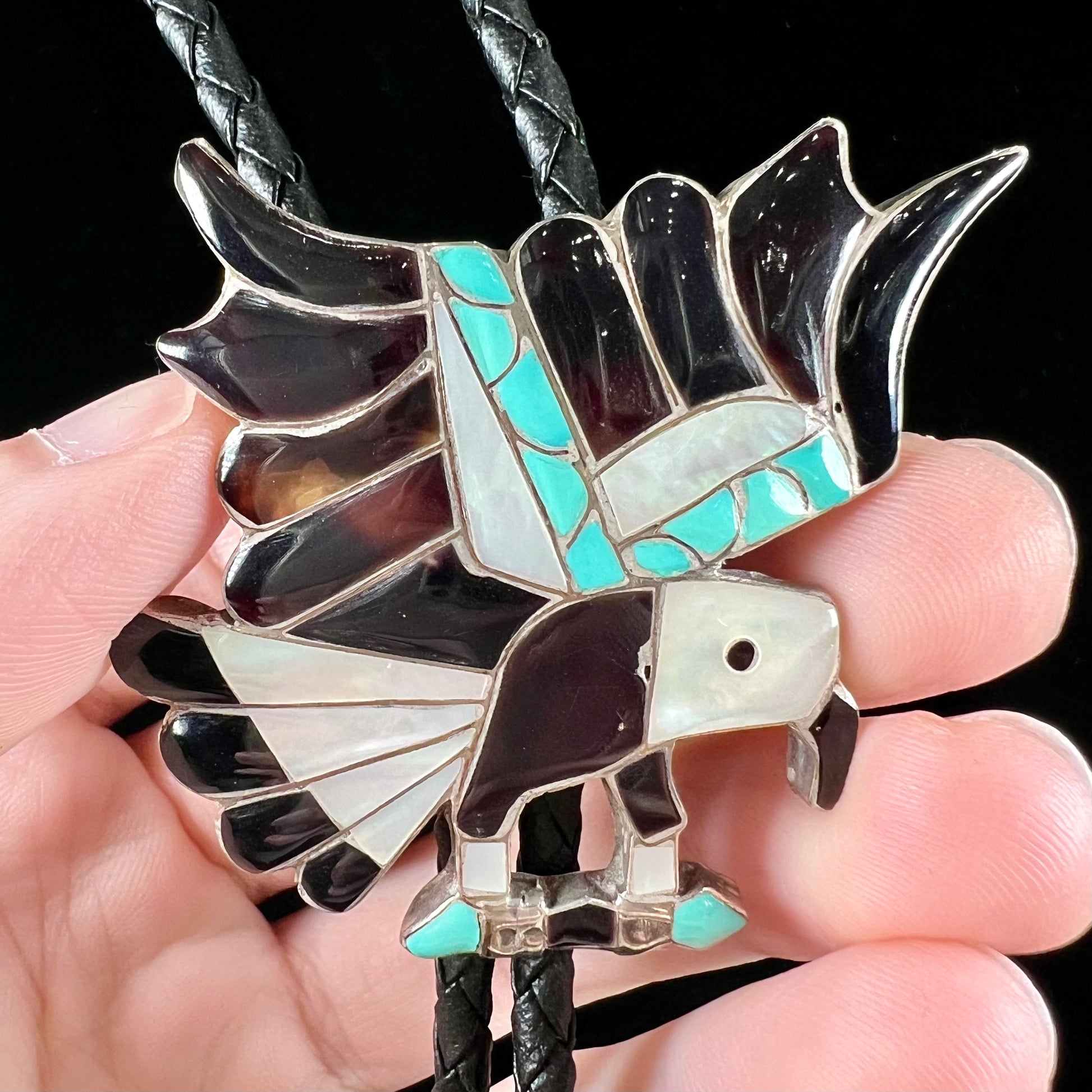 A sterling silver Zuni Indian-made bolo tie featuring the motif of three flying eagles inlaid with natural stones.