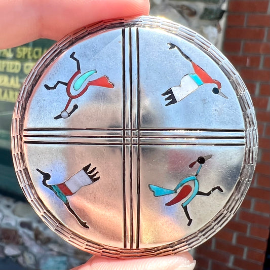 A silver pendant of two flying cranes and two roadrunners inlaid with turquoise, coral, and mother of pearl.