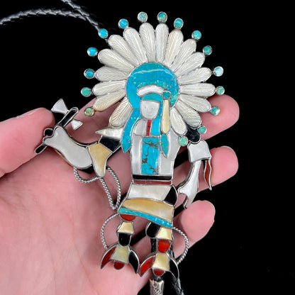 A Zuni Indian-made bolo tie featuring the motif of a kachina, inlaid with natural turquoise, mother of pearl, jet, and jasper stones.