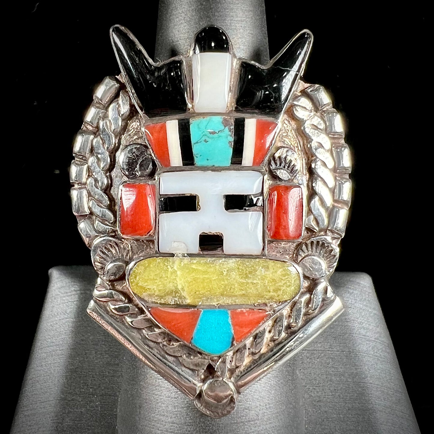 A sterling silver ring handmade in the motif of a Zuni Indian horned kachina set with onyx, turquoise, coral, mother of pearl, and sulfur quartz stones.