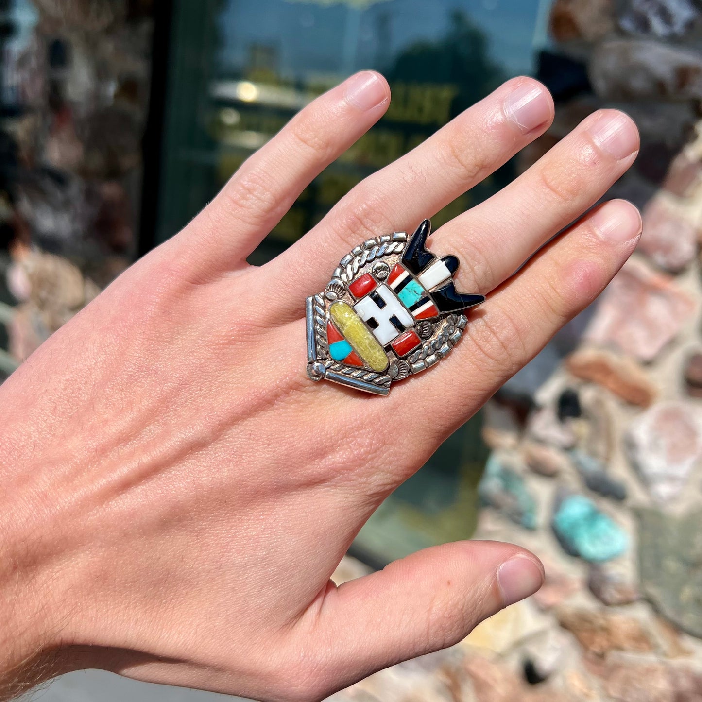 A sterling silver ring handmade in the motif of a Zuni Indian horned kachina set with onyx, turquoise, coral, mother of pearl, and sulfur quartz stones.