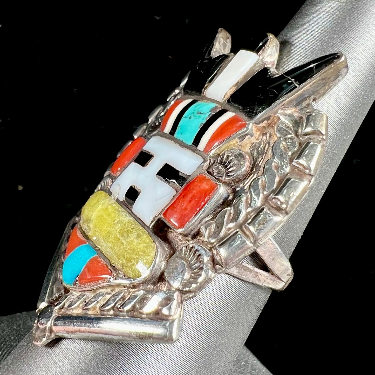 A sterling silver ring handmade in the motif of a Zuni Indian horned kachina set with onyx, turquoise, coral, mother of pearl, and sulfur quartz stones.