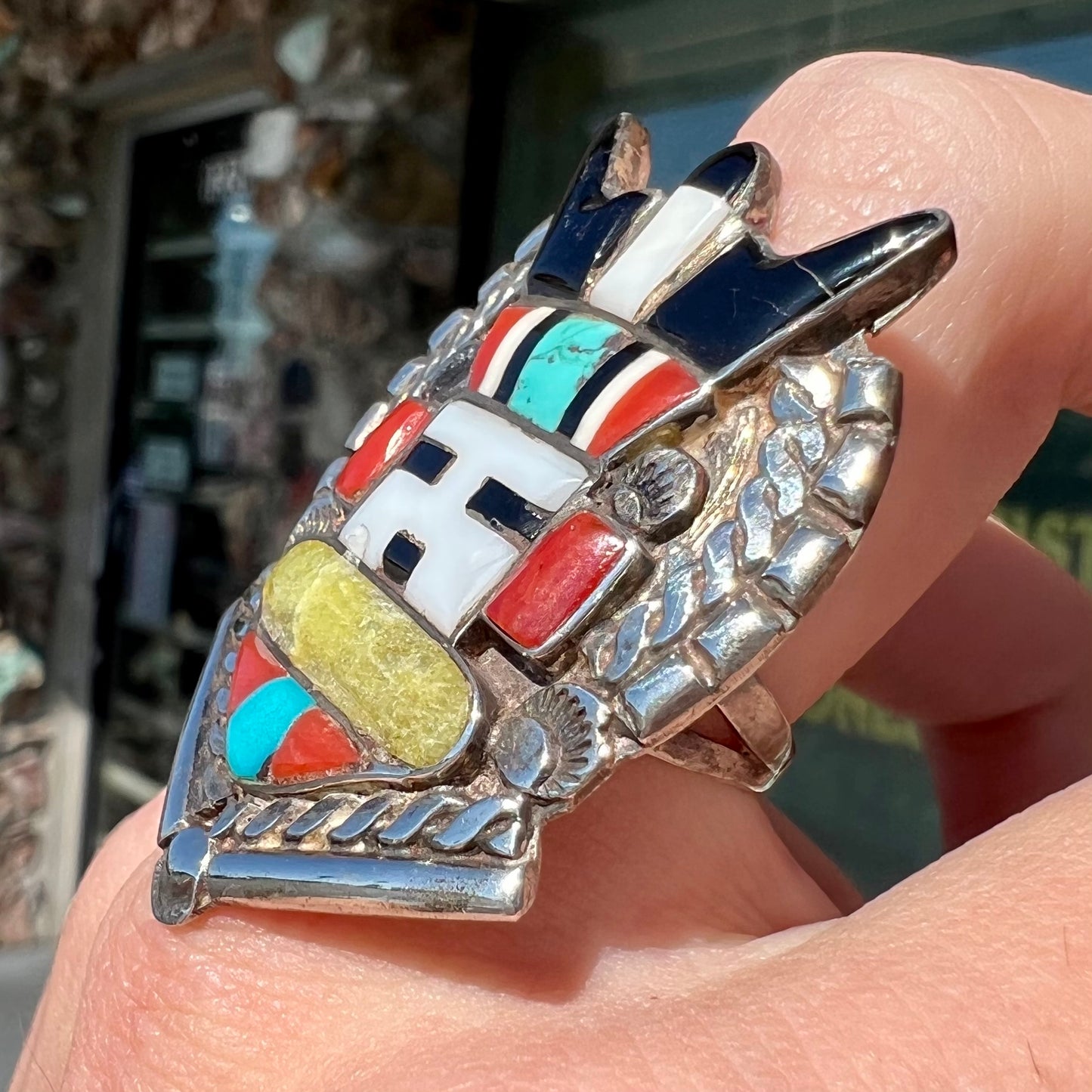 A sterling silver ring handmade in the motif of a Zuni Indian horned kachina set with onyx, turquoise, coral, mother of pearl, and sulfur quartz stones.