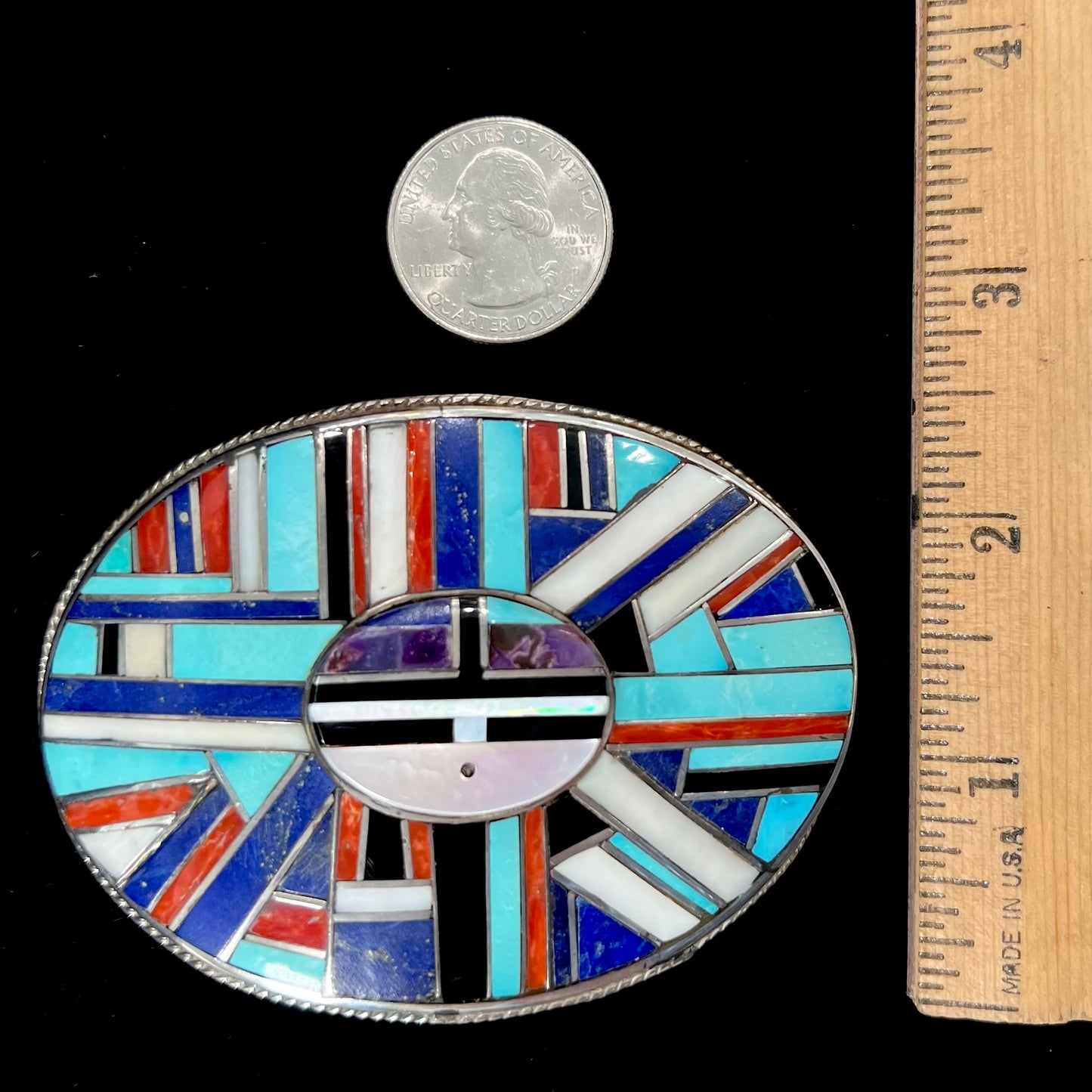 A sterling silver Zuni sunface belt buckle inlaid with lapis, turquoise, onyx, mother of pearl, coral, and sugilite stones.  It is stamped "RGB Zuni."