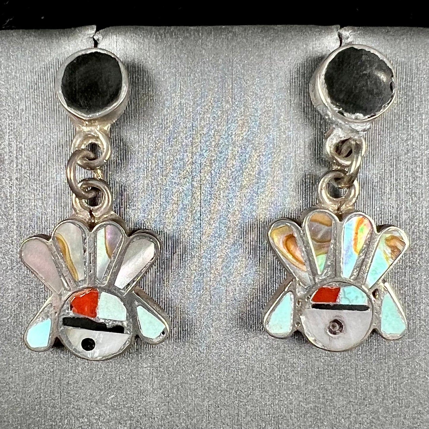 A pair of dangle earrings depicting the motif of Zuni Indian Sunfaces, inlaid with mother of pearl, onyx, turquoise, and coral.