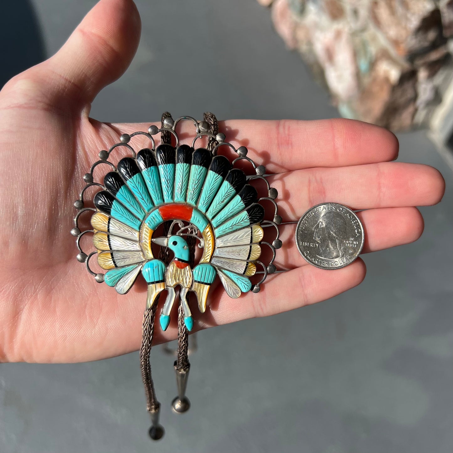 A handmade Zuni style stone inlay peacock bolo tie set with onyx, coral, turquoise, and gold lipped pearl on a silver bolo chain.