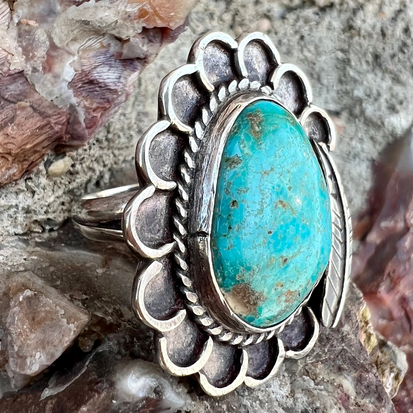 A sterling silver Navajo style ring.  The ring is set with a turquoise stone from Pilot Mountain.  There is a feather decoration next to the stone.